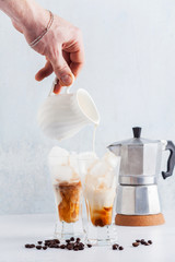 a man's hand pours milk in cold brew coffee on the table. coffee pot in the background