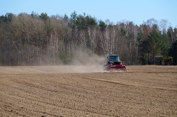 Fototapeta premium The tractor harrows fields for cultivation. Spring field work.