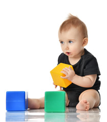 Infant child baby toddler sitting in dress with green blue and yellow brick toy playing isolated on a white