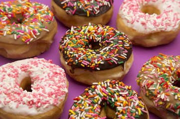 A Background of Various Sprinkle Donuts on a Purple Background