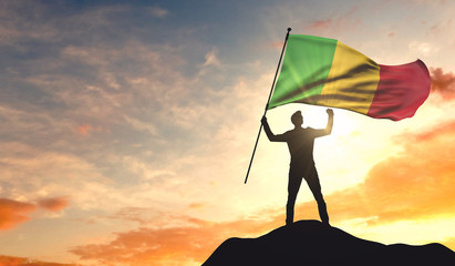 Mali flag being waved by a man celebrating success at the top of a mountain. 3D Rendering - obrazy, fototapety, plakaty