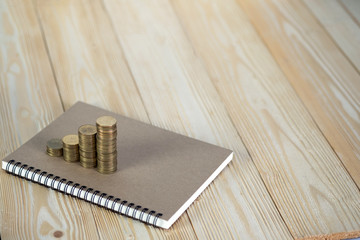 Steps of coins stack with notebook paper on wooden working table with copy space for text, financial and business planning concept.