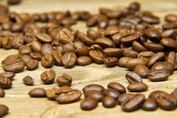 Coffee beans spilled onto a wood table with the focus on the beans in the middle.