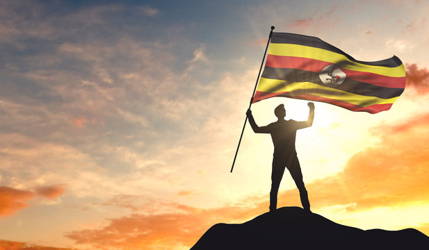 Uganda flag being waved by a man celebrating success at the top of a mountain. 3D Rendering