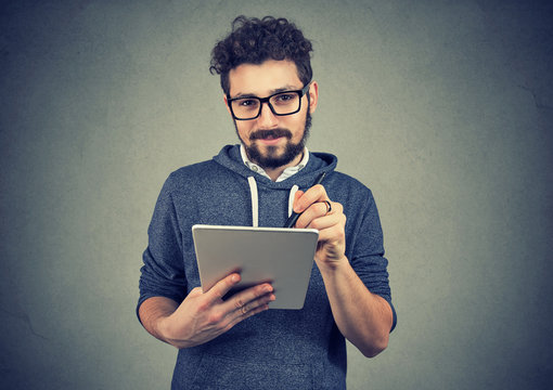 Hispter man in glasses holding tablet computer and pen looking at camera