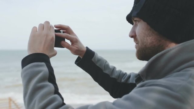 Young caucasian man taking photos of sea at storm 