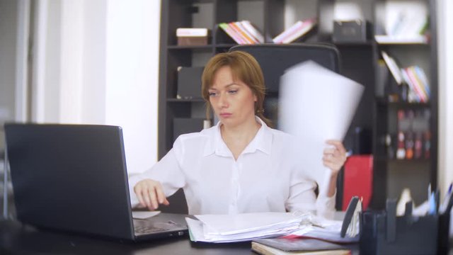 a businesswoman who scans documents, frowns, using a laptop, does not perform an urgent task in the office, there is not enough time, 4k. the office is hot, the air conditioning is not working