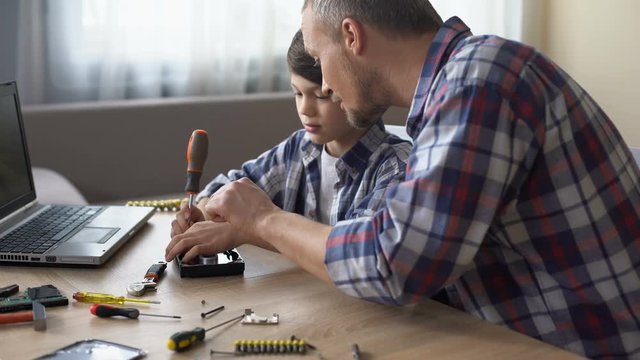 Caring father teaching his little son to repair hard disk drive at home, hobby