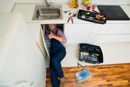 Handsome Guy Lying On Floor Repairing Sink In Kitchen