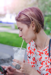 The girl is drinking a cocktail and looking into the phone