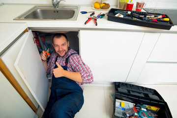 Handyman Lying On Floor Repairing Sink In Kitchen