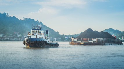 tugboats pull heavy load barge of black coal in Mahakam river, Borneo, Indonesia
