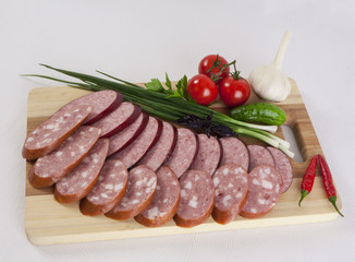 still life with sliced smoked sausage greens and tomatoes on a white background