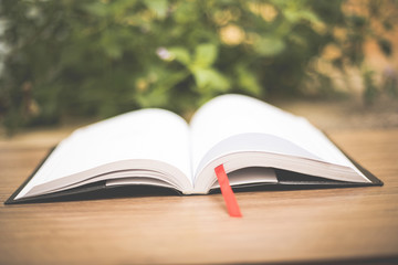 An open book on  wooden table at home garden with nature bokeh background