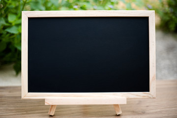 Black board on wood table top with sun and blur green tree bokeh background, Template mock up for display of product