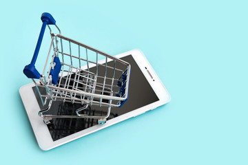 Tablet computer and small cart for shopping on cyan background. Internet shopping concept. copy space.