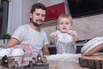 A tiny sweet girl with blond hair spends time with her dad, cooking in the kitchen. Preparations for the holidays. Baking.