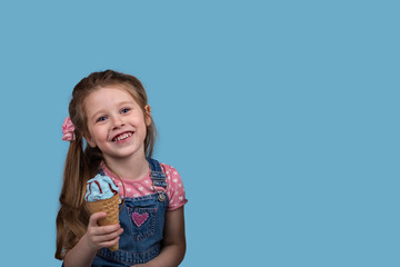  The little girl  cheerfully eats ice cream in wafer gunny on blue background in studio.