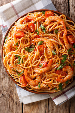 Italian pasta spaghetti with prawns, parmesan and herbs in tomato diavolo sauce close-up. Vertical top view