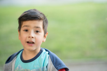 Close up emotional portrait of the smiling of the little boy   wearing  grey jacket in a park.