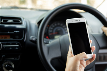 Woman hand holding mobile phone sending a text while driving a car. Selective focus.