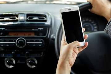 Woman hand holding mobile phone sending a text while driving a car. Selective focus.
