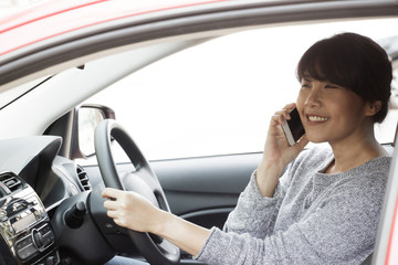 Young asian woman in casual wear driving a car, using smart phone and  looking on road. Risky driving. Woman sitting in car with cell phone