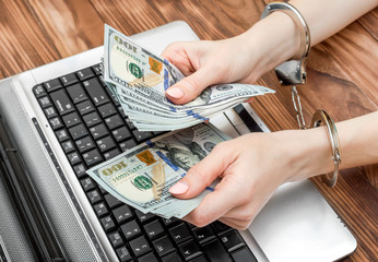Female holding money in hands which are locked up by handcuffs over laptop.