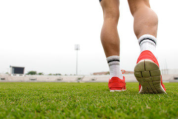Sports background. Runner feet running on green lawn close up on red shoe.