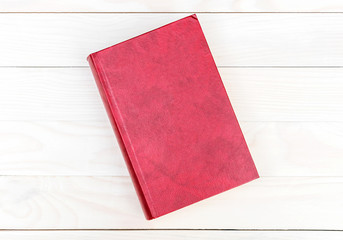 Closed blank red book on wooden table. Top view.