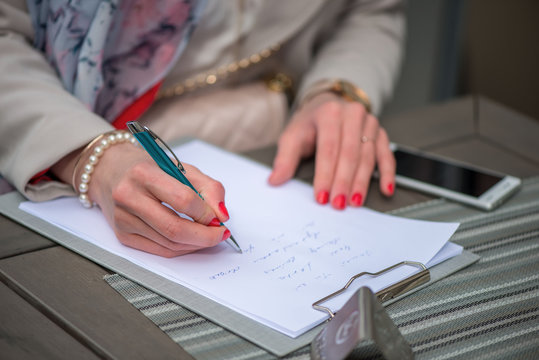 Close-up of female hands. Woman writing something sitting at cafe. Signing documents.