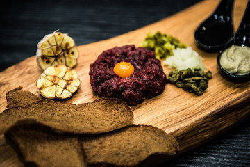 Beef tartare with pickled cucumber and fresh onions on dark  background, selective focus
