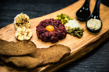 Beef tartare with pickled cucumber and fresh onions on dark  background, selective focus