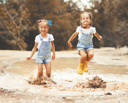 Happy funny sisters twins child girl   jumping on puddles in rubber boots  .