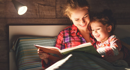 mother and child reading book in bed before going to sleep .