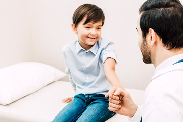Obraz premium Doctor holding hand little boy with care on doctors table in hospital.healthcare and medicine