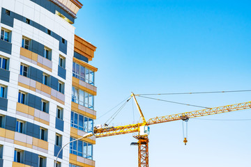 Construction crane against bright blue sky near a construction site of a residential building high-rise