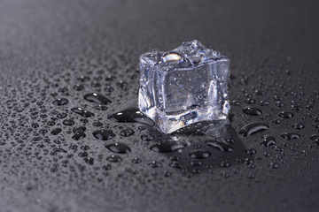 Single ice cube with water drops isolated on black background