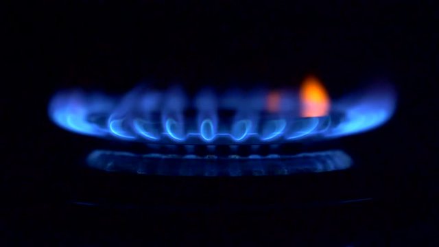 Gas is switching on, apearing blue flame. Gas stove on black background. 