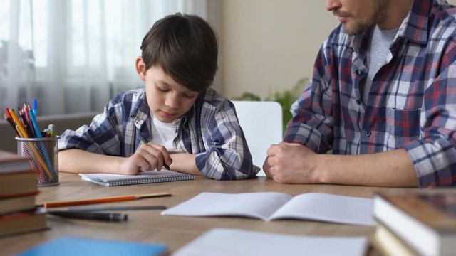 Father scolding son, making him to do homework, boy beginning to write task
