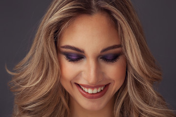 Lovely blonde woman smiling with eyes closed while wearing purple eyeshadow - obrazy, fototapety, plakaty