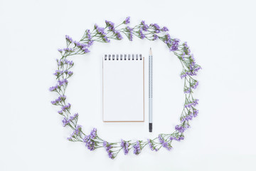 Top view of blank notebook with pencil in floral frame of flowers on whitedesk background, flat lay.