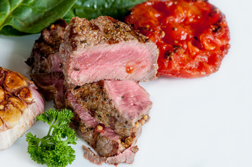 Steak rare with the blood of vegetables tomatoes and spinach grilled in a white plate at home on a light background. Close up.