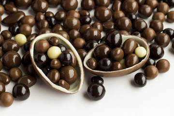 Dark and brown ball chocolates in shell of chocolate egg on the ball chocolates on white with copy space.Conceptual image of celebrations.