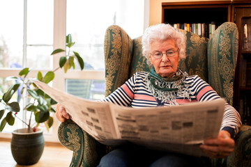 Senior woman in pansion relaxing at home while reading a newspaper