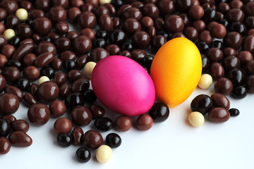 Pink and yellow Easter eggs on white with dark ball chocolates.Conceptual image of Easter Holiday