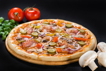 Appetizing pizza with salami, mozzarella, pepper, olives and pickled cucumbers on wooden board on dark background