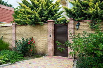 entrance house group with a wicket and stone fence surrounded by green bushes and trees, horizontal frame