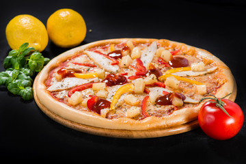 Appetizing pizza with salami, mozzarella, pepper, chicken, sauce on wooden board on dark background