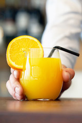 Close-up image of a men hand holding glass of orange juice. The barman gives glasses of orange juice to the client of the hotel restaurant. The waiter transfers orange juice to the client.